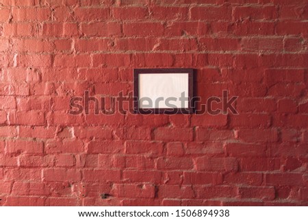 A framed blank picture hanging on a red brick wall