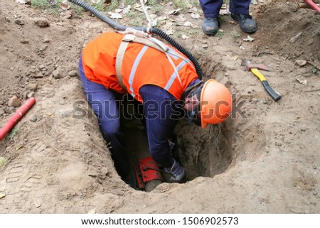 worker in the ground repairs the pipe