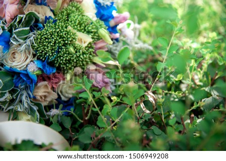 Two gold wedding rings hanging on a twig of a green Bush with the bride's wedding bouquet on the background