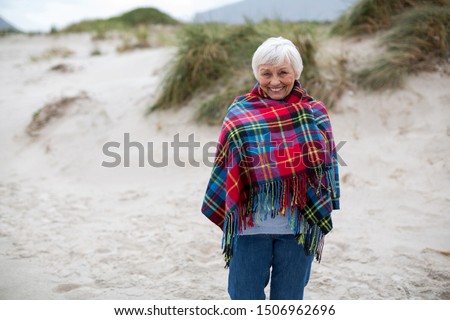 Portrait of smiling senior woman wrapped in shawl on the beach