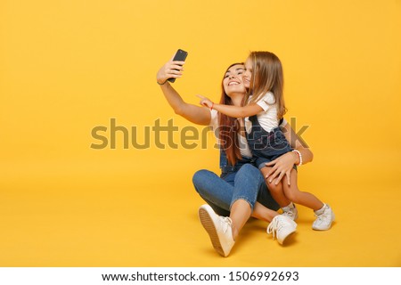 Woman in light clothes doing selfie with cute child baby girl 4-5 years old. Mommy little kid daughter isolated on yellow background studio portrait. Mother's Day family parenthood childhood concept