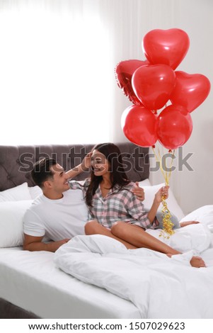 Beautiful couple with heart shaped balloons in bedroom