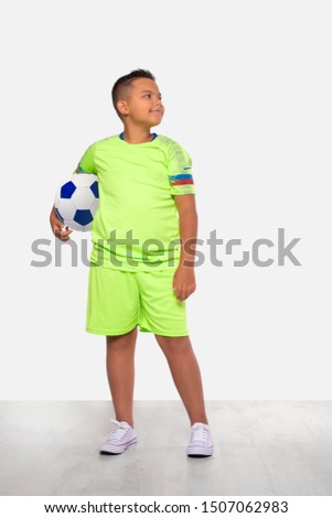 Studio portrait of a positive smiling mixed race boy in green football uniform and with ball on a white background