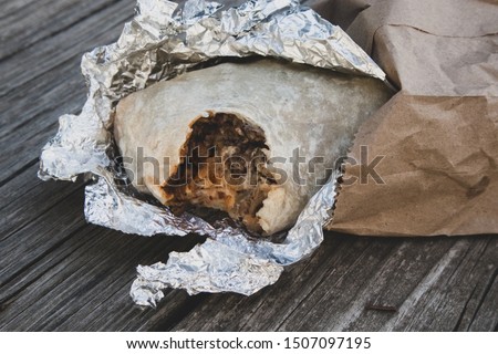 Burrito with a Bite Out of It in Foil and Paper Sack