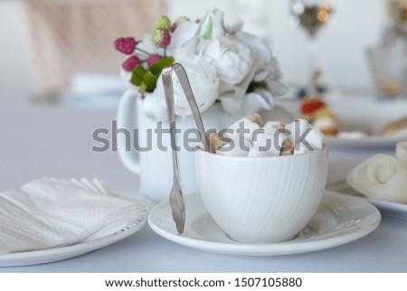 A Cup filled with lump sugar with tongs on a white tablecloth. A fragment of the interior