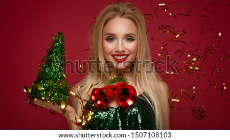 Beautiful blonde girl in a New Year's image with Christmas bells around her neck and green tree. Beauty face with festive makeup. Photo taken in the studio.