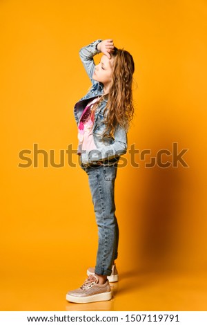 Young teen girl model posing on a yellow background in jeans and a jacket. with long hair gathered in a high tail