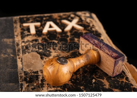 Inscription tax on an old book and stamp. Office accessories on a dark table. Black background.