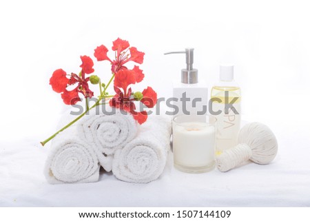 Spa setting with red flower with petals, flowers lies on  rolled towel with herbal ball,oil bottle,candle 