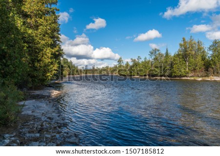 Picturesque Early Fall picture of very scenic river rapids featuring river rocks, shore, trees in early fall on a blue sky sunny day