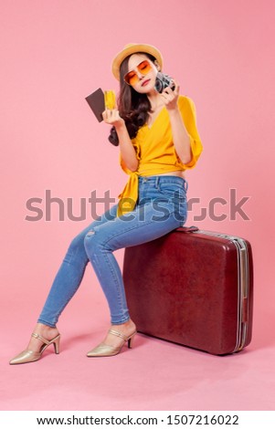 Smiling woman traveler sitting on luggage holding camera passport credit card in holiday on pink backgrounds, relaxation concept, travel concept