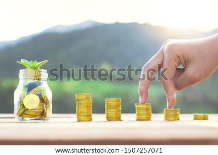 Website banner of golden coins in a glass jar with hand walking on coin stack at sunset background