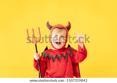 Funny child dressed devil costume against yellow background. Happy Halloween holidays concept