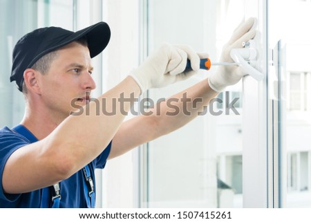 the hands of a worker fasten the handle to a plastic window,  view from the side Royalty-Free Stock Photo #1507415261