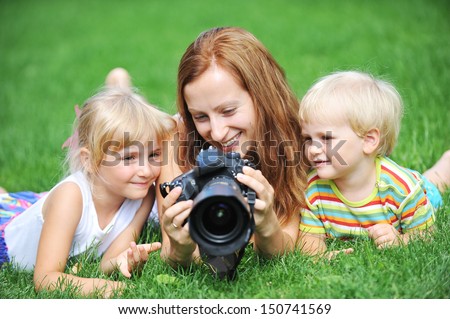 young mother with her children lie on grass and looking at screen of camera. summer day.