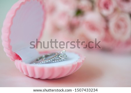 Close up of elegant ring in the shell box with coral roses on watercolor background. Selective focus. Love and wedding concept.