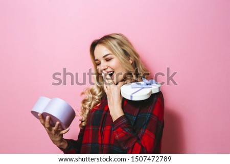 Image of a young  beautiful blonde girl holding a gift and happy on a pink background