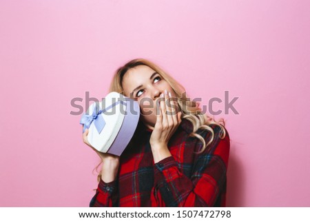 Image of a young  beautiful blonde girl holding a gift and happy on a pink background