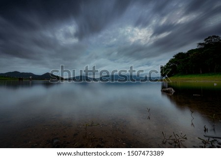 Beautiful landscape of reservoir in the morning. Mountain and green tree forest. Cloudy sky. Clear water in the river. Fresh air. Clean environment. White and dark cloudscape. Village in valley.