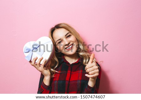 Image of a  beautiful blonde girl holding a gift and happy over pink background