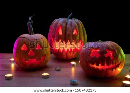 Halloween pumpkin head jack-o-lantern with scary evil faces and candles. Seasonal illuminated decoration. Looks scary, colorful neon light and dark background. Holidays. Black friday, sales.