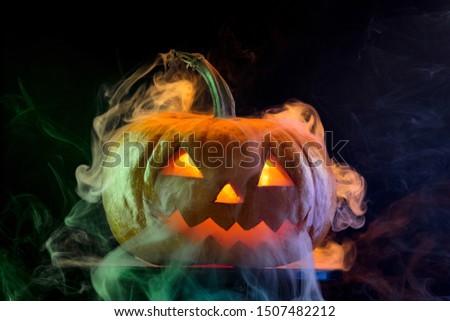 Halloween pumpkin head jack-o-lantern with scary evil face. Seasonal illuminated decoration. Looks scary, neon light, white smoke and dark background. Holidays. Black friday, sales. Night of fear.