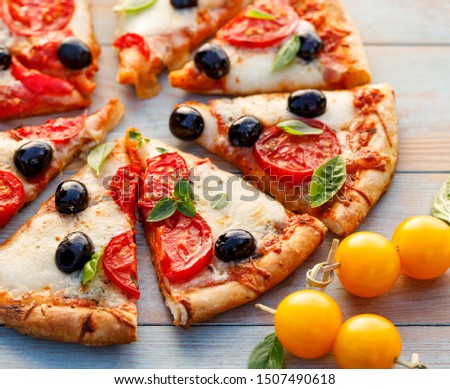 Pizza, sliced pizza with tomatoes, black olives,  mozzarella cheese and fresh basil on a wooden background, close up. Italian food