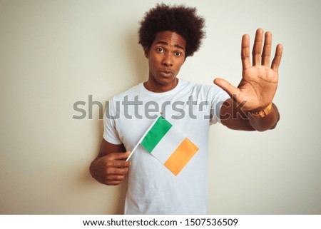 Young african american man holding Ireland Irish flag standing over isolated white background with open hand doing stop sign with serious and confident expression, defense gesture