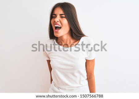 Young beautiful woman wearing casual t-shirt standing over isolated white background angry and mad screaming frustrated and furious, shouting with anger. Rage and aggressive concept.