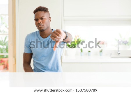 Handsome african american man wearing casual t-shirt at home looking unhappy and angry showing rejection and negative with thumbs down gesture. Bad expression.