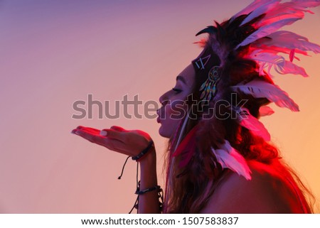 Portrait in profile of nice woman in headdress of feathers sanding air kiss isolated over violet neon background
