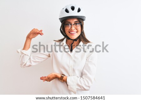 Beautiful businesswoman wearing glasses and bike helmet over isolated white background gesturing with hands showing big and large size sign, measure symbol. Smiling looking at the camera.