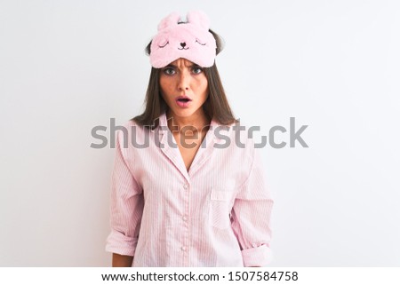 Young beautiful woman wearing sleep mask and pajama over isolated white background afraid and shocked with surprise and amazed expression, fear and excited face.