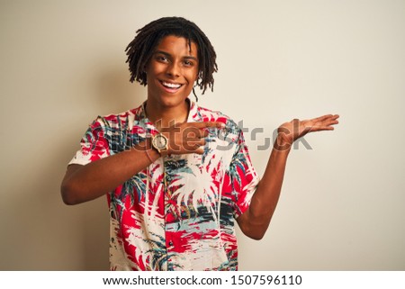 Afro man with dreadlocks on vacation wearing summer shirt over isolated white background amazed and smiling to the camera while presenting with hand and pointing with finger.