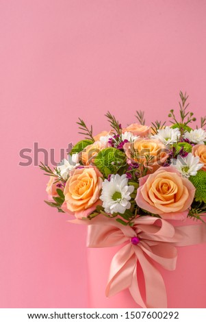 Beautiful bouquet in a coral luxury present box with a pink bow, isolated on pink background