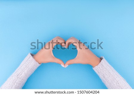 Beautiful woman is hands with a perfect manicure making the heart on blue background. Flat lay style. Top view. Place for design.