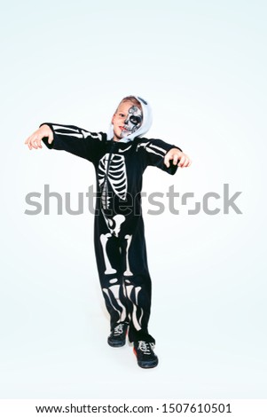 Little boy like a vampire in scary black costume with bones on white background. Caucasian male model looks scary. Halloween, black friday, sales, autumn holidays concept. The night of fear.