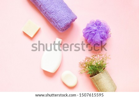 Purple rolled towel, white soap bar, sponge and flowers on a pink background. Flat lay beauty photography. Natural organic bath products for skin and hair care
