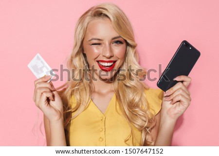 Image of pleased woman with long blond hair smiling while holding cellphone and credit card isolated over pink background