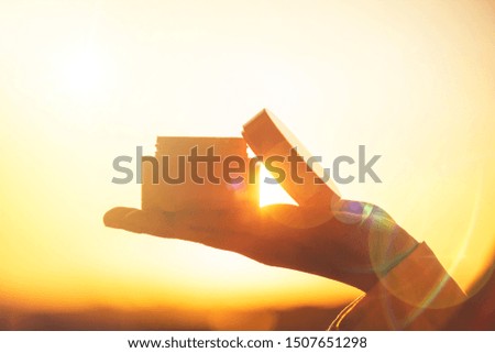 woman applying night hand cream using jar standing near window at the evening on the sunset background. Sun rays. Beam. Concept.