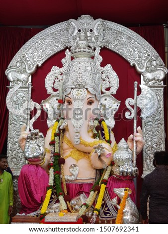 silver statue of lord ganesh wearing silver crown, jewellery, holding modak, trident, trisul in his hands, silver rat mouse seated near ganpati isolated on silver indian design and red background.