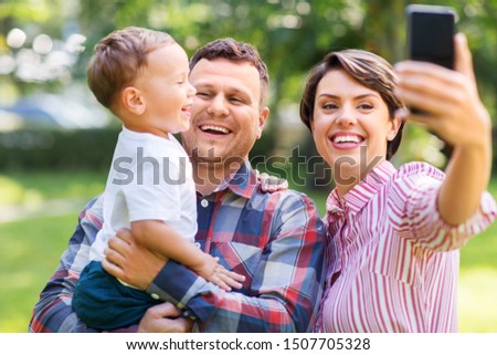 family, leisure and people concept - happy mother, father and little son taking selfie by smartphone at summer park