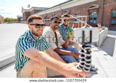 leisure, technology and people concept - happy male friends taking selfie by smartphone on tripod and drinking beer on street in summer