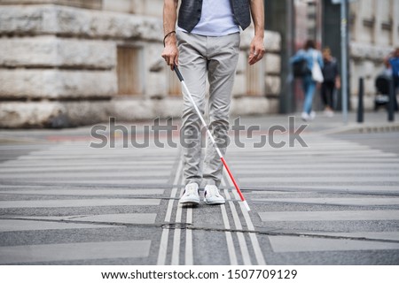 Midsection of young blind man with white cane walking across the street in city. Royalty-Free Stock Photo #1507709129