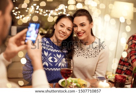 holidays and celebration concept - happy friends having christmas dinner at home and taking picture by smartphone