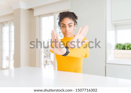 Beautiful african american woman with afro hair wearing a casual yellow sweater Rejection expression crossing arms and palms doing negative sign, angry face