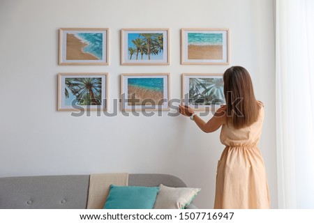 Female interior designer decorating white wall with pictures indoors