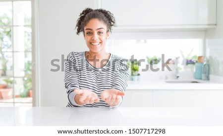 Beautiful african american woman with afro hair wearing casual striped sweater Smiling with hands palms together receiving or giving gesture. Hold and protection