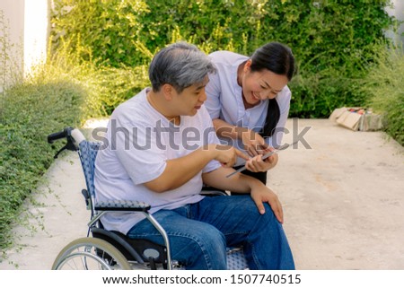 Male patient sitting on a wheelchair use tablet with wife in the garden with happiness