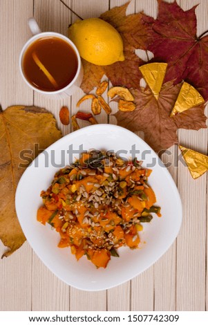cup of tea with lemon and pumpkin stew with vegetables on an autumn background, maple leaves and dry apples on a wooden table, top view